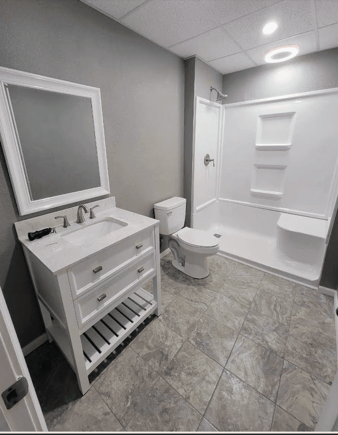 Modern bathroom featuring a white vanity, mirror, toilet, and walk-in shower against gray walls.