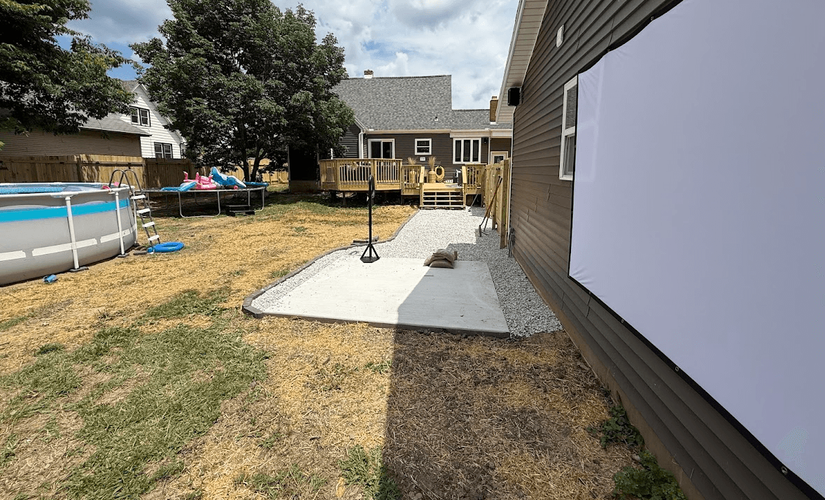 White movie screen on a house wall beside a concrete patio and backyard swimming pool.