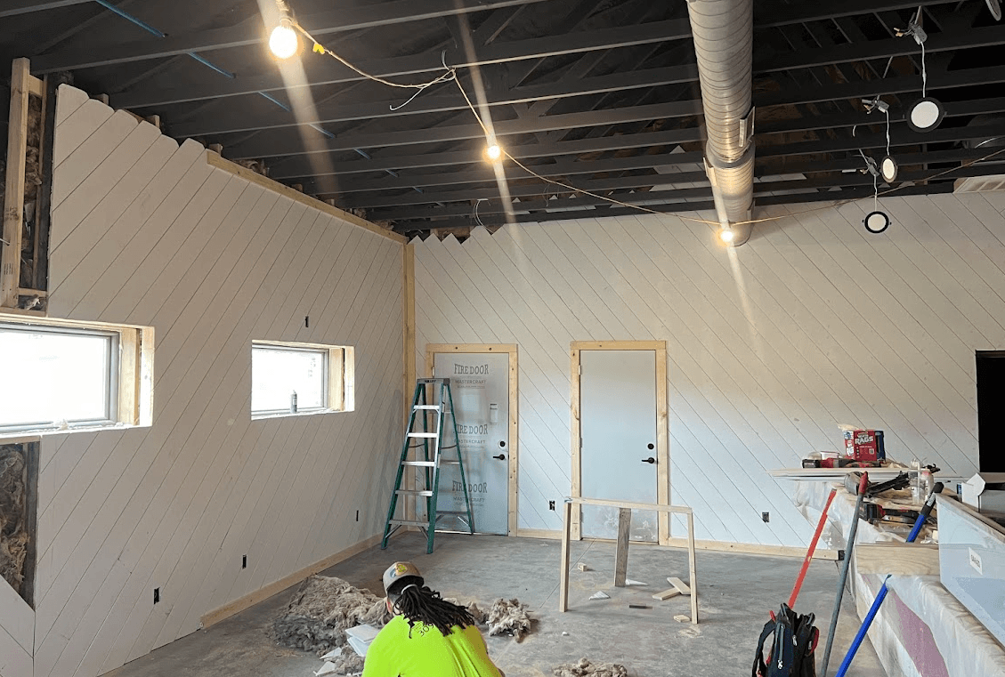 Interior renovation featuring white diagonal wood paneling, exposed ceiling joists, and construction tools.
