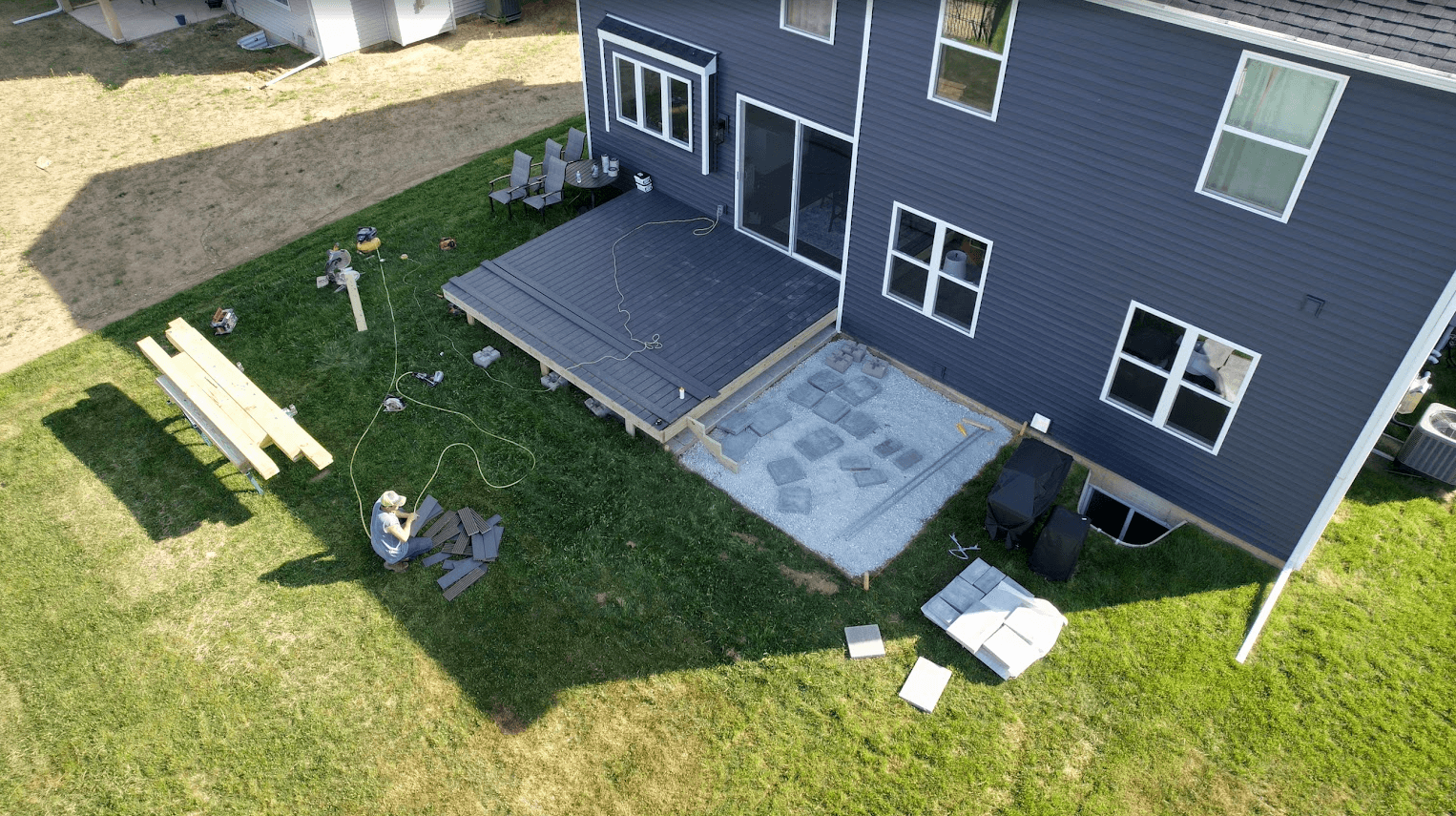 Aerial view of a worker building a grey deck and patio behind a blue house.